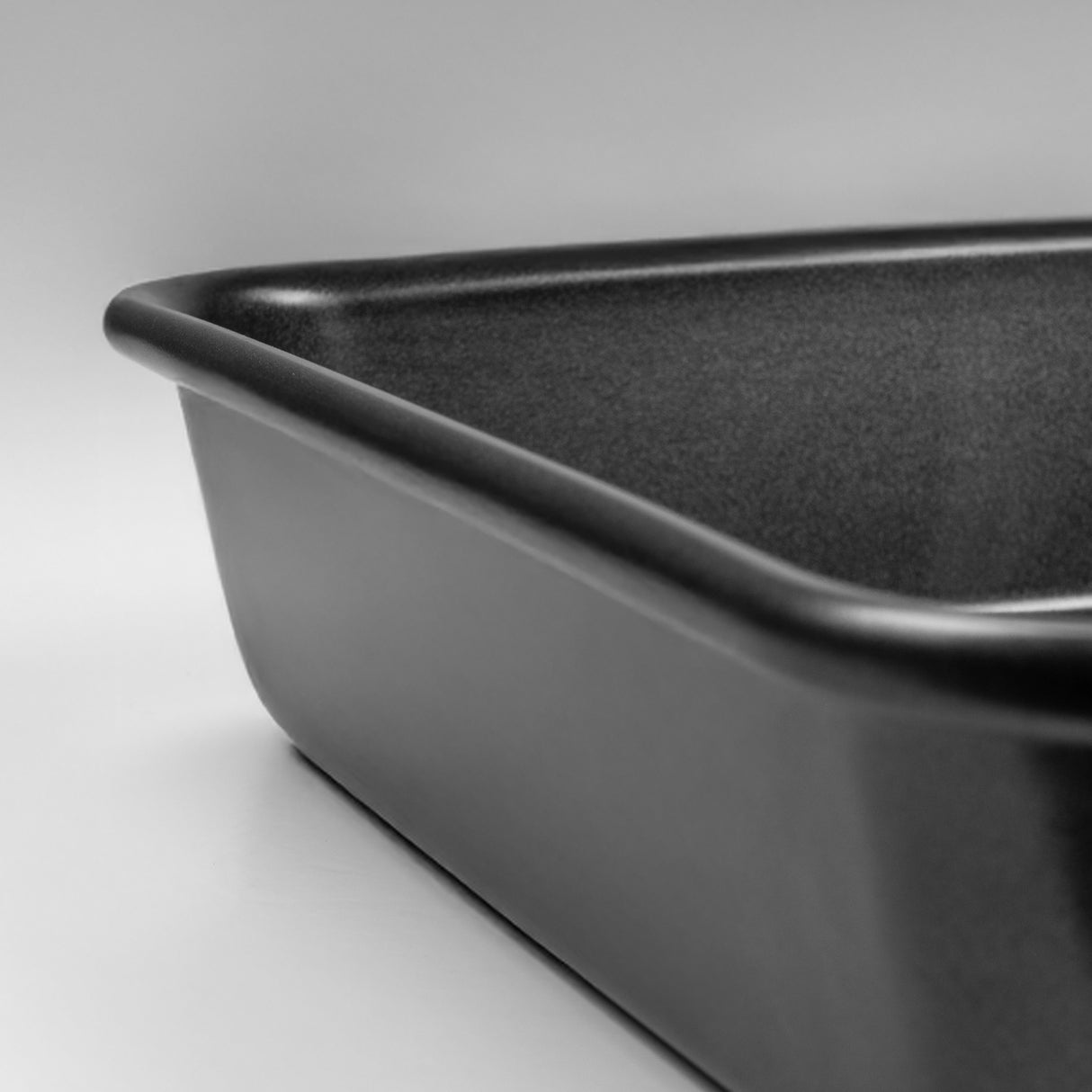 Close up shot of a black carbon steel square cake tin on a light grey background