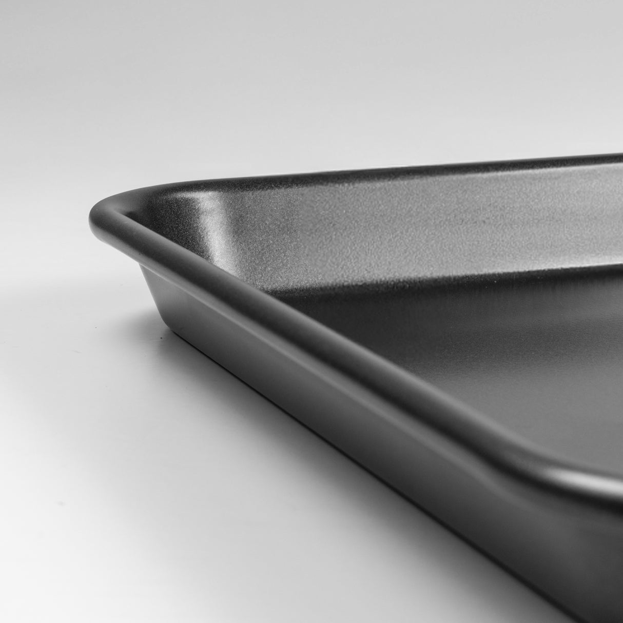 Close up shot of a black carbon steel rectangular baking tray with rounded corners on a light grey background