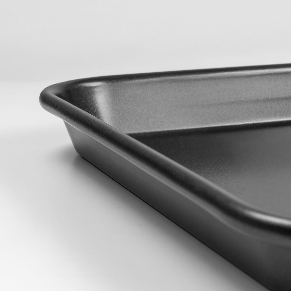 Close up shot of a black carbon steel rectangular baking tray with rounded corners on a light grey background