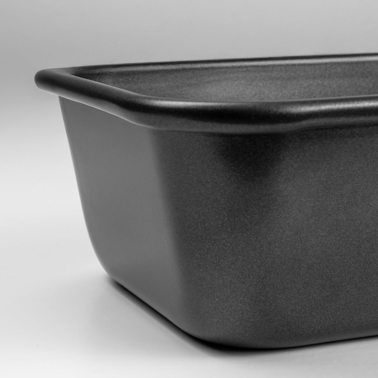 Close up shot of a black carbon steel rectangular roasting tin on a light grey background