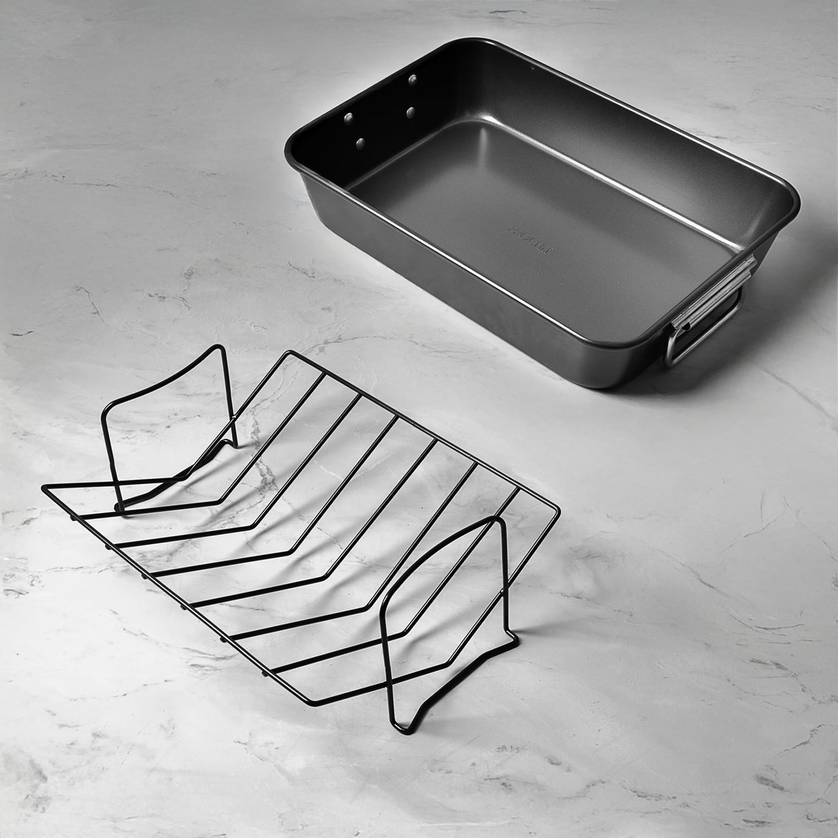 ProChef black carbon steel roasting tin with a V-rack next to it on a light grey marble countertop