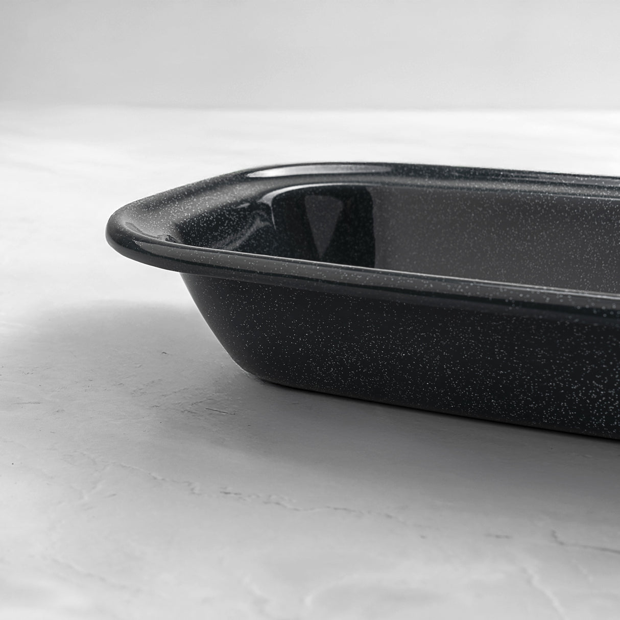 Close-up of a rectangular grey speckled enamel pie dish, showing deep sides and smooth enamel finish for oven baking.