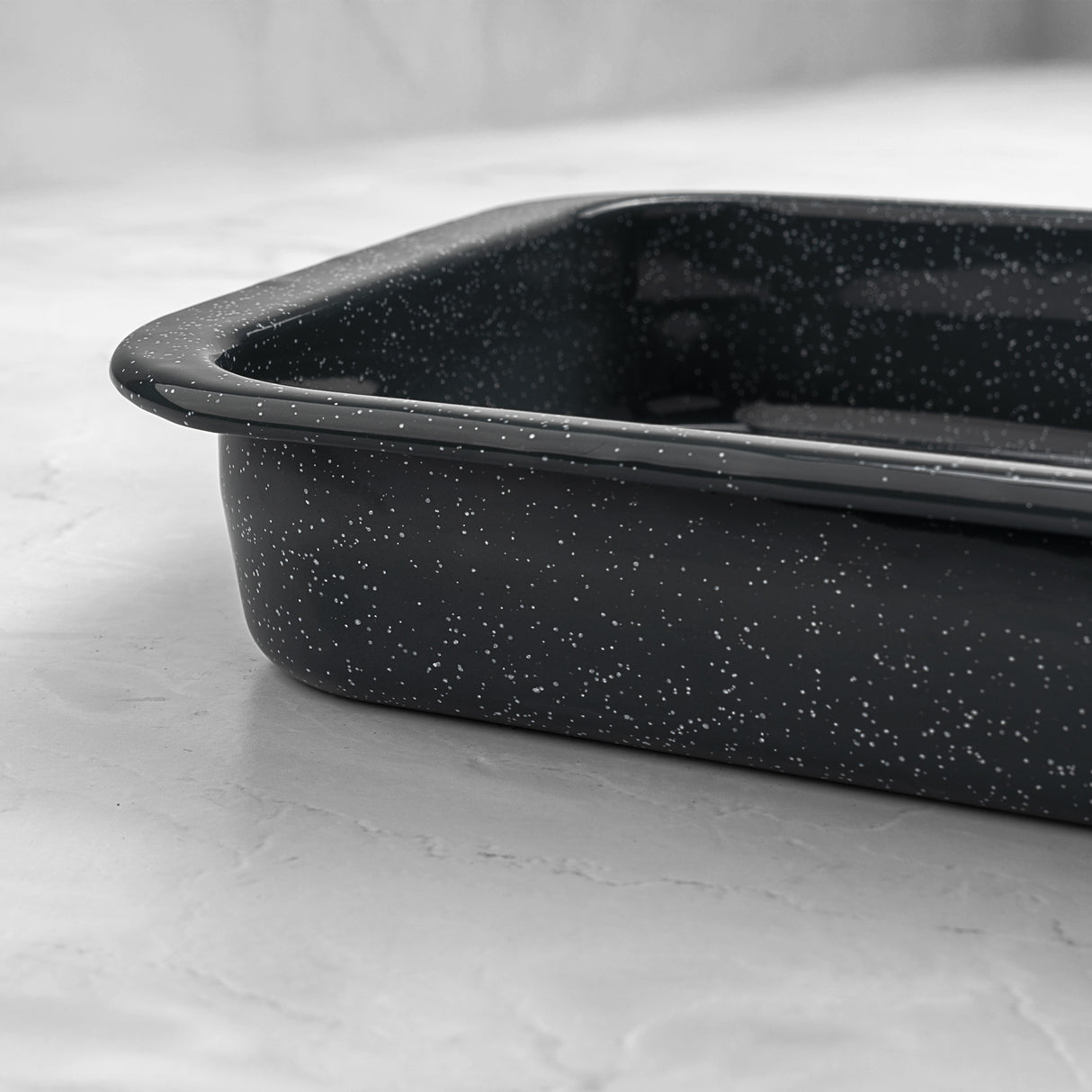 Side view of a rectangular grey speckled enamel roasting dish on a marble surface.
