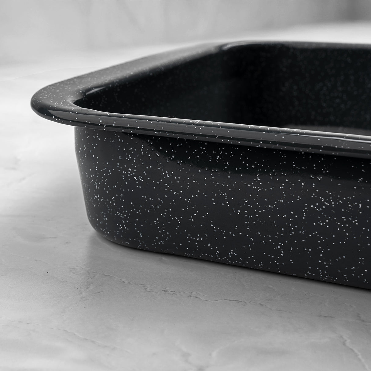 Close up of a grey speckled enamel roasting tin on a light grey surface