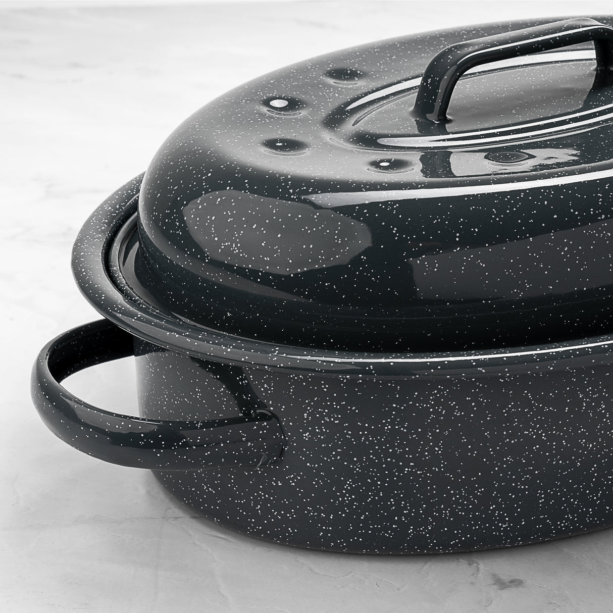 Grey speckled enamelled cast iron roaster with lid on a light grey background