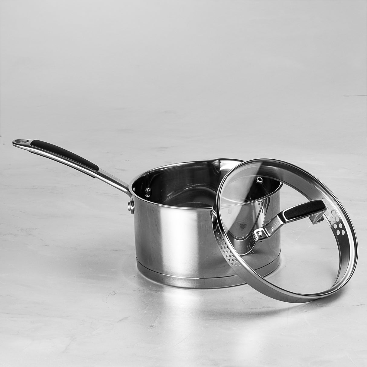 Stainless steel saucepan with lid on a light gray background