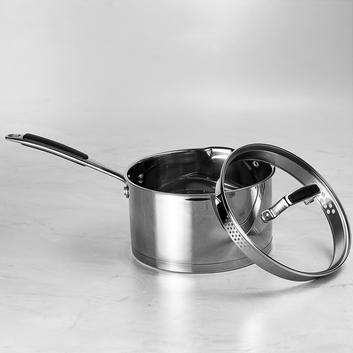 Stainless steel saucepan with lid on a light gray background