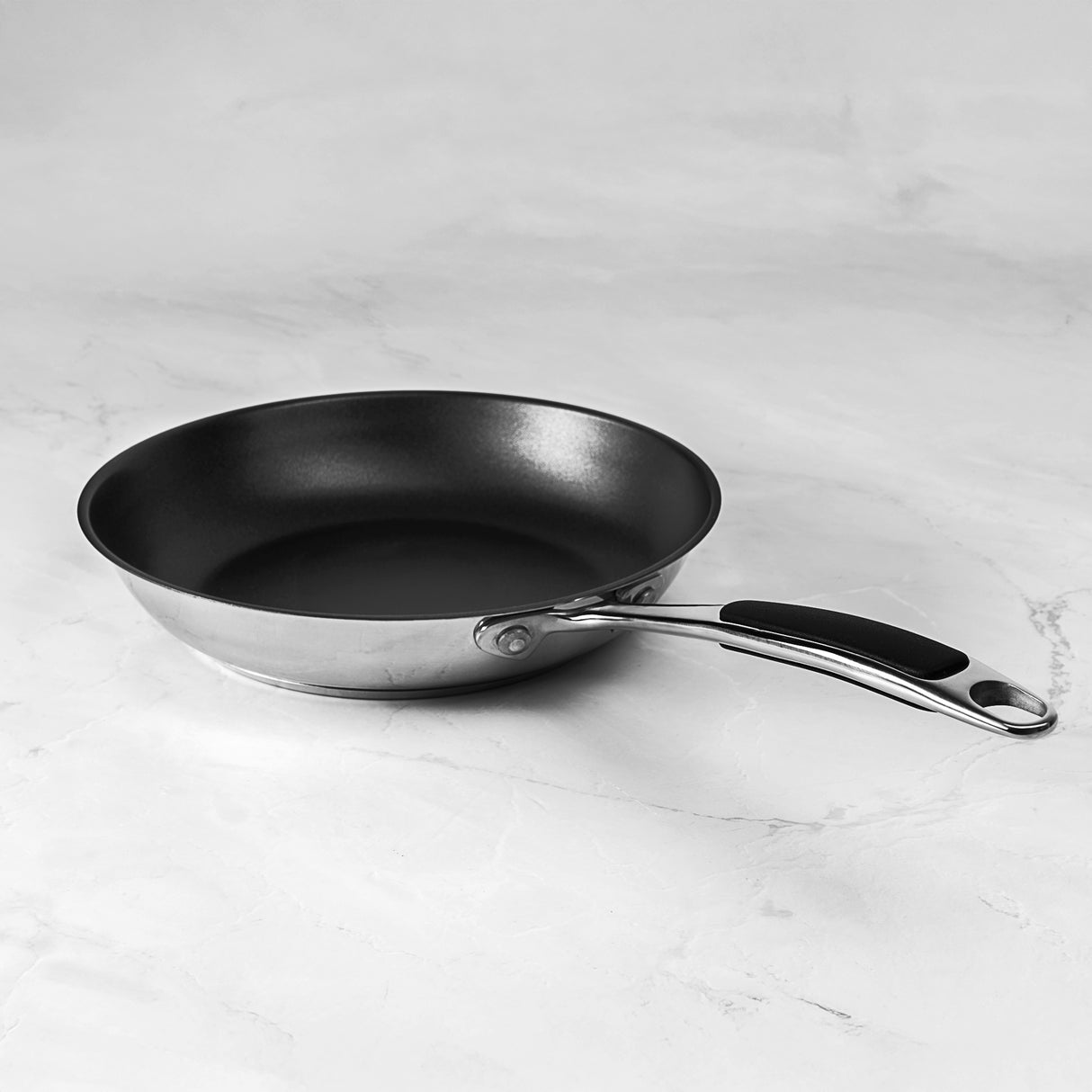 Silver frying pan on a light gray marble surface