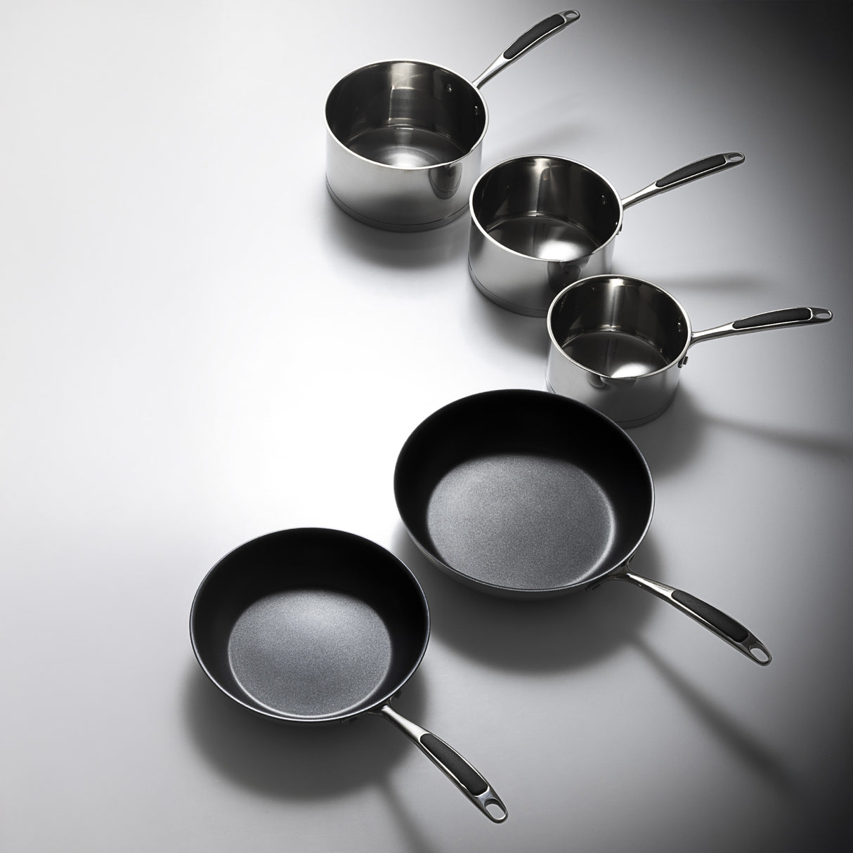 Set of stainless steel cookware including pots and pans on a gray background