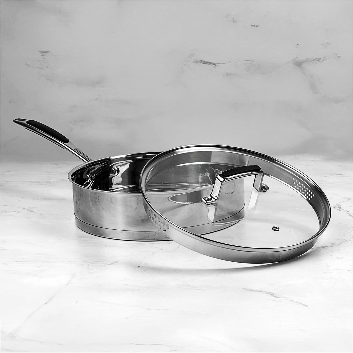 Stainless steel sauté pan with lid on a marble surface