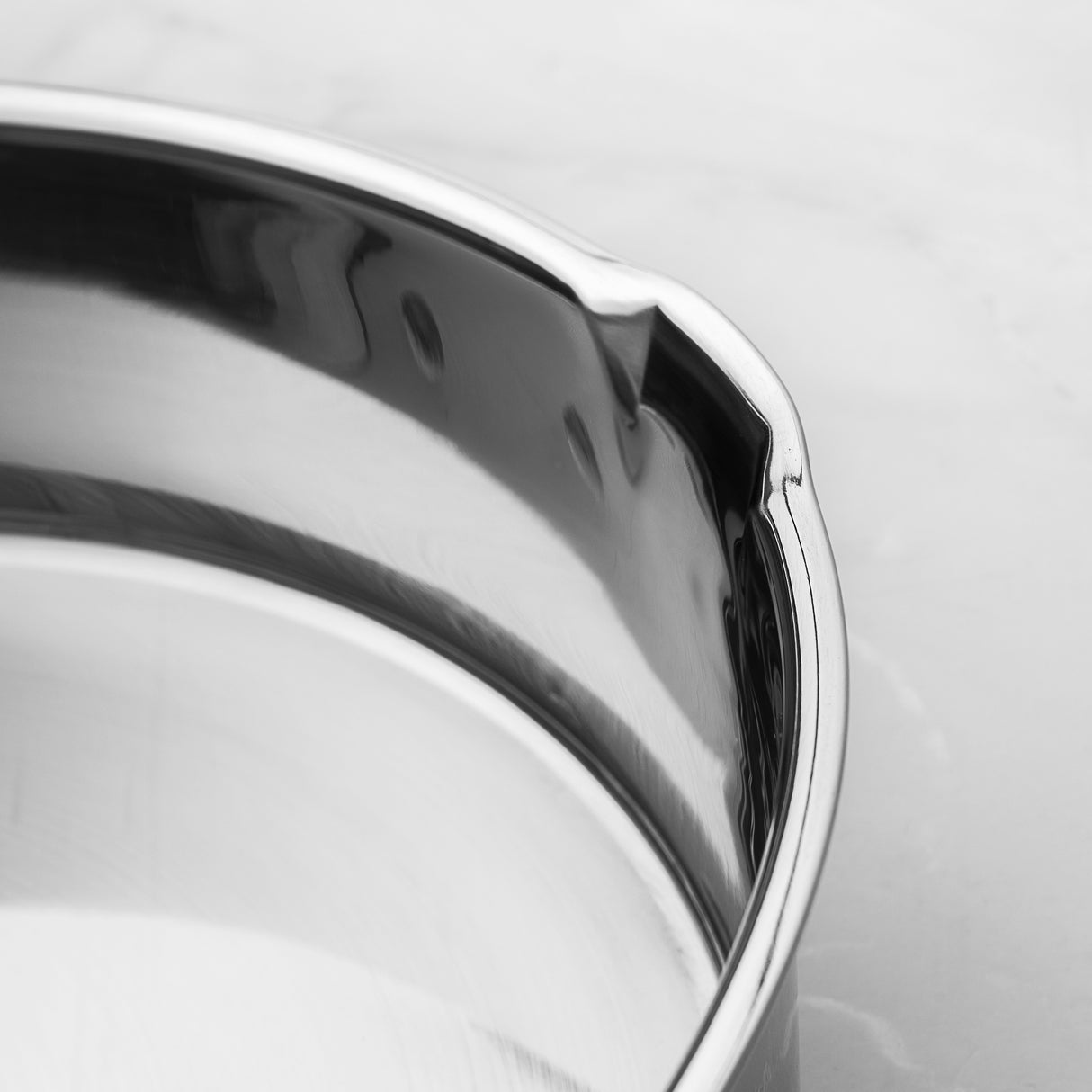 Close-up of a shiny metal rim on a stainless steel pan with a blurred background