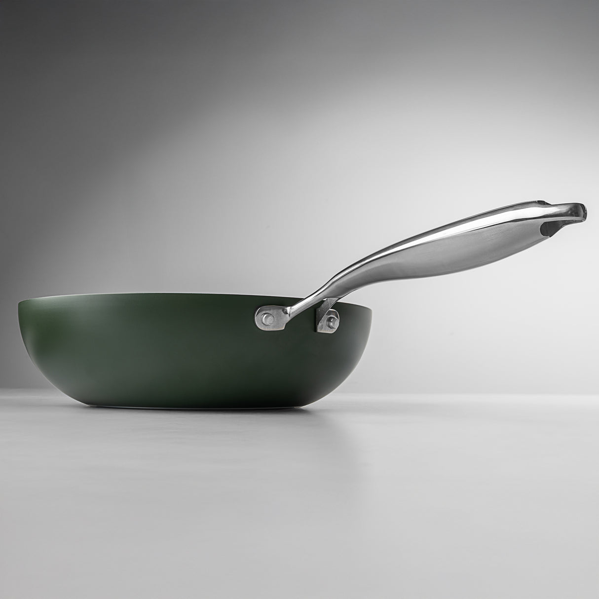 Green frying pan with a silver handle on a gray background