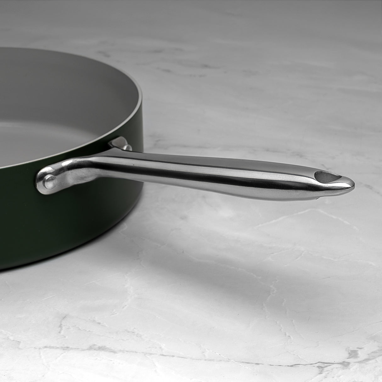 Green saute pan with a silver handle on a marble surface