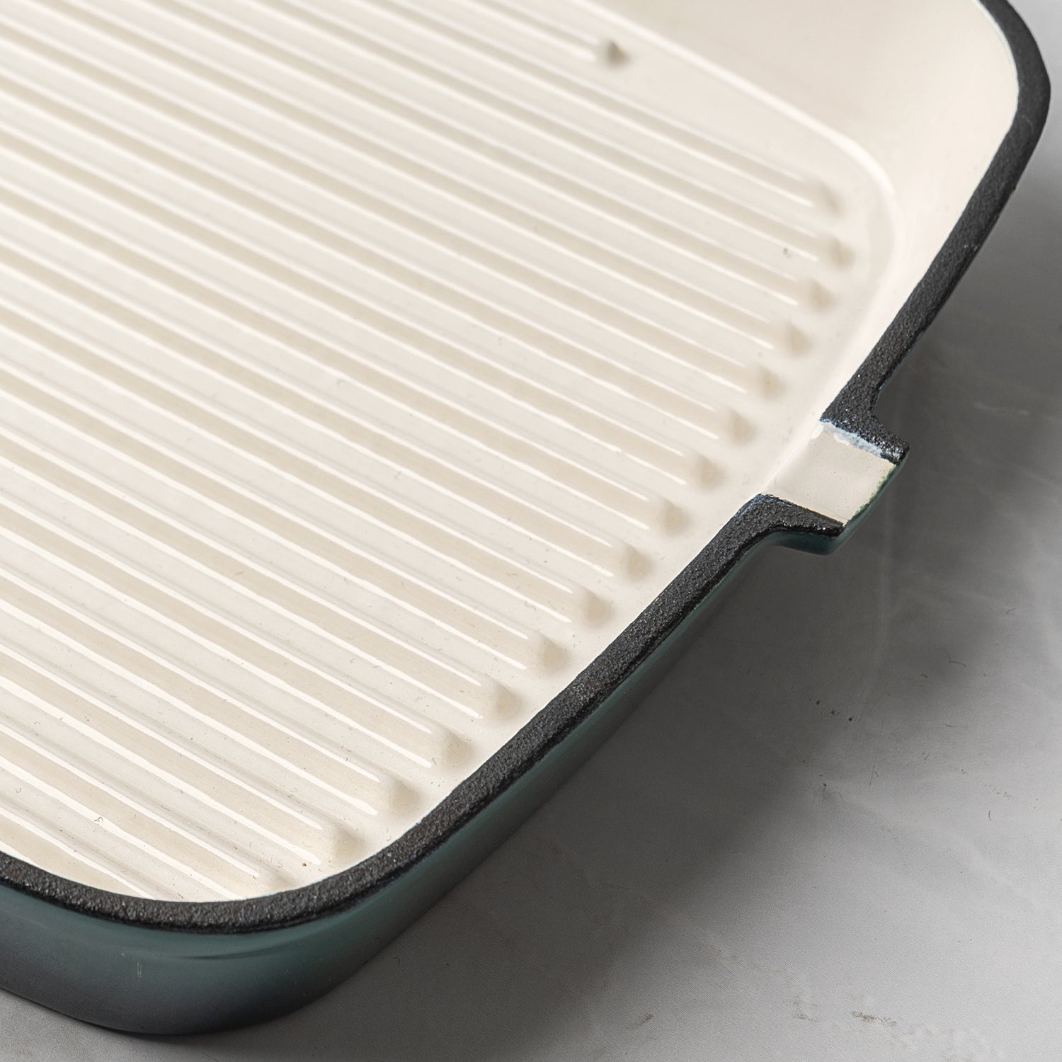 Close-up of ProChef enamelled cast iron square griddle pan in teal with cream interior and ridged base for searing.