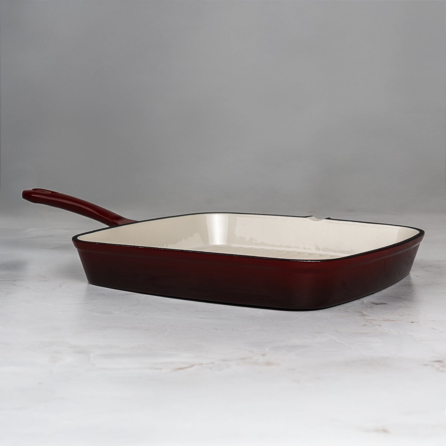 Square enameled cast iron skillet with red-brown exterior and white interior on a light gray background