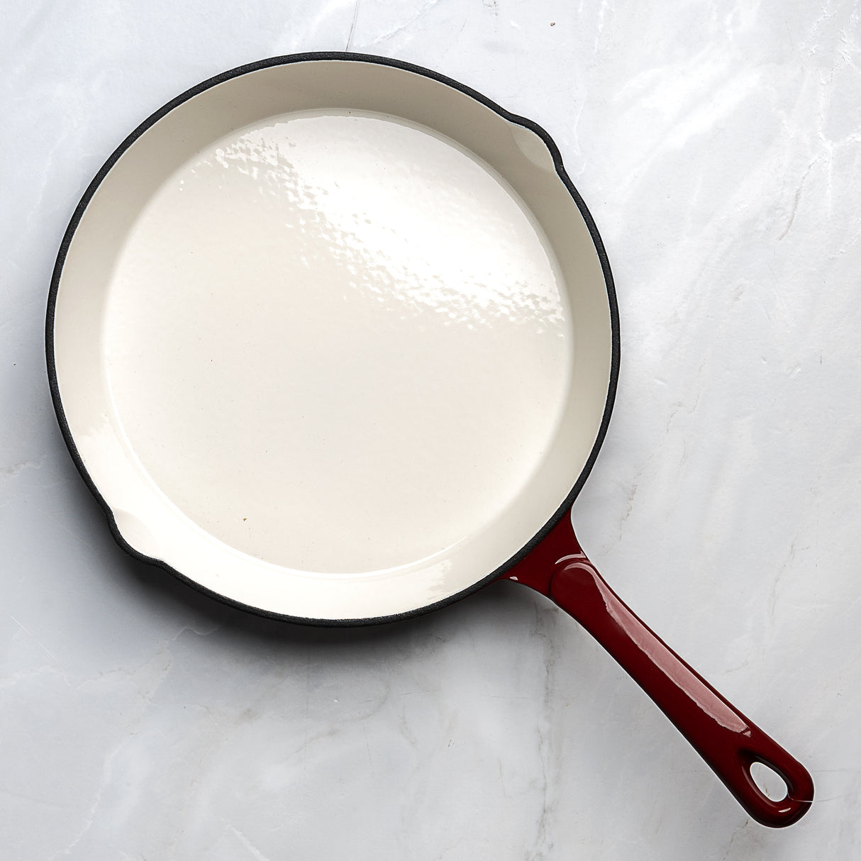 Cast iron skillet with red handle on a white marble surface