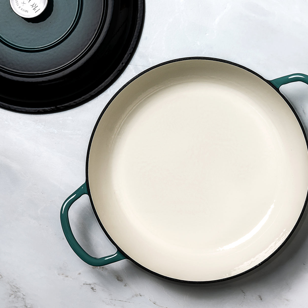 ProChef shallow cast iron casserole in teal with white enamel interior, shown from above with matching black-and-teal lid placed to the side.