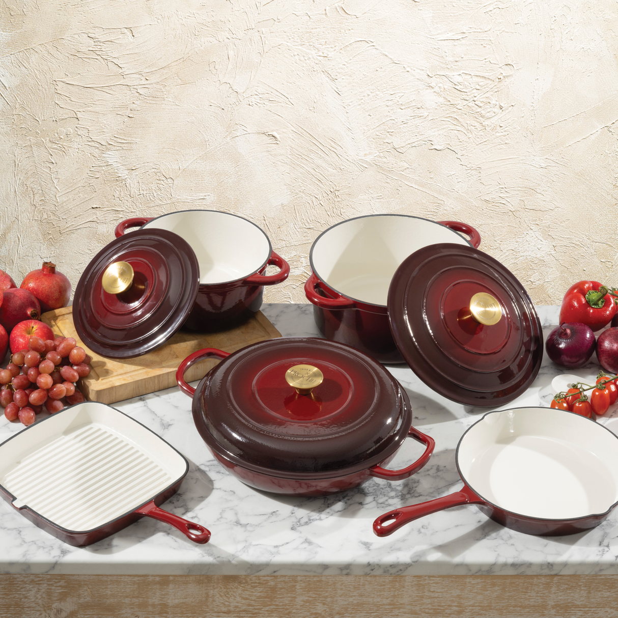 Set of red ProChef cast iron cookware with white interiors on a marble surface with fruits and vegetables.