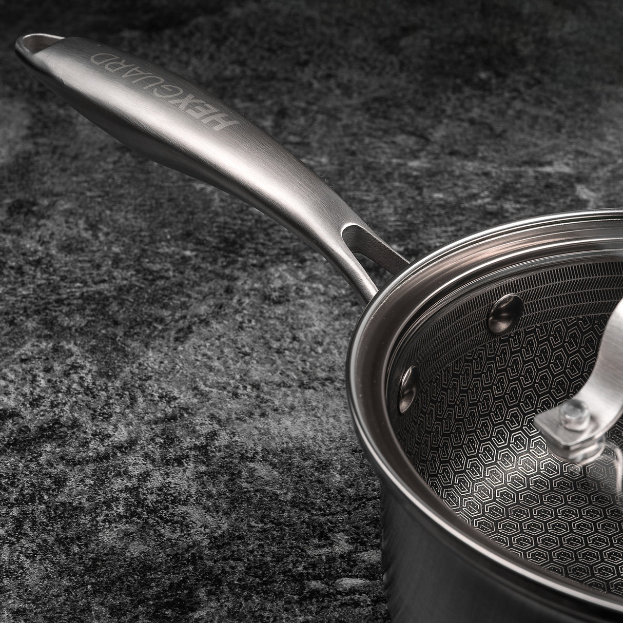 Stainless steel saucepan with lid on a dark textured surface