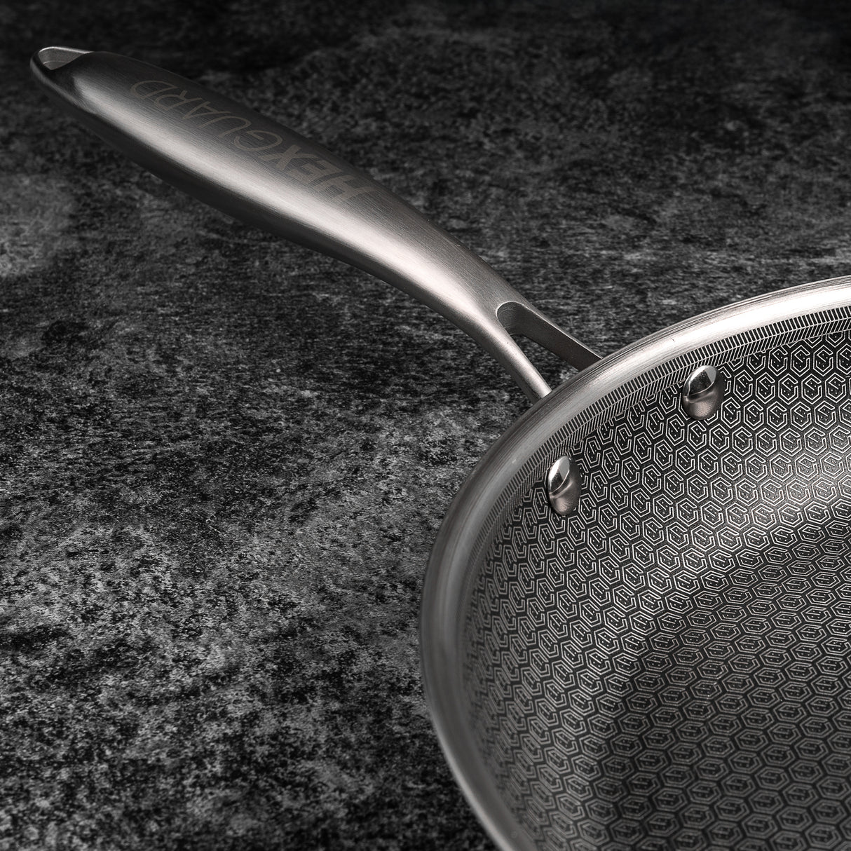 Silver frying pan with hexagonal pattern on a dark surface