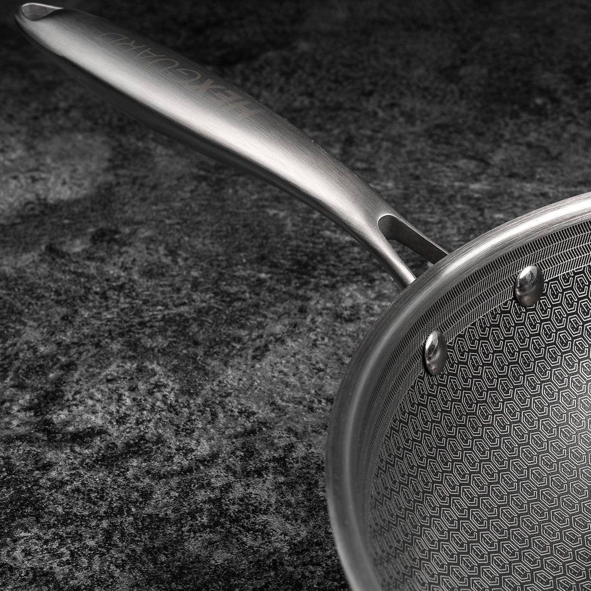 Stainless steel frying pan with geometric pattern on a dark surface