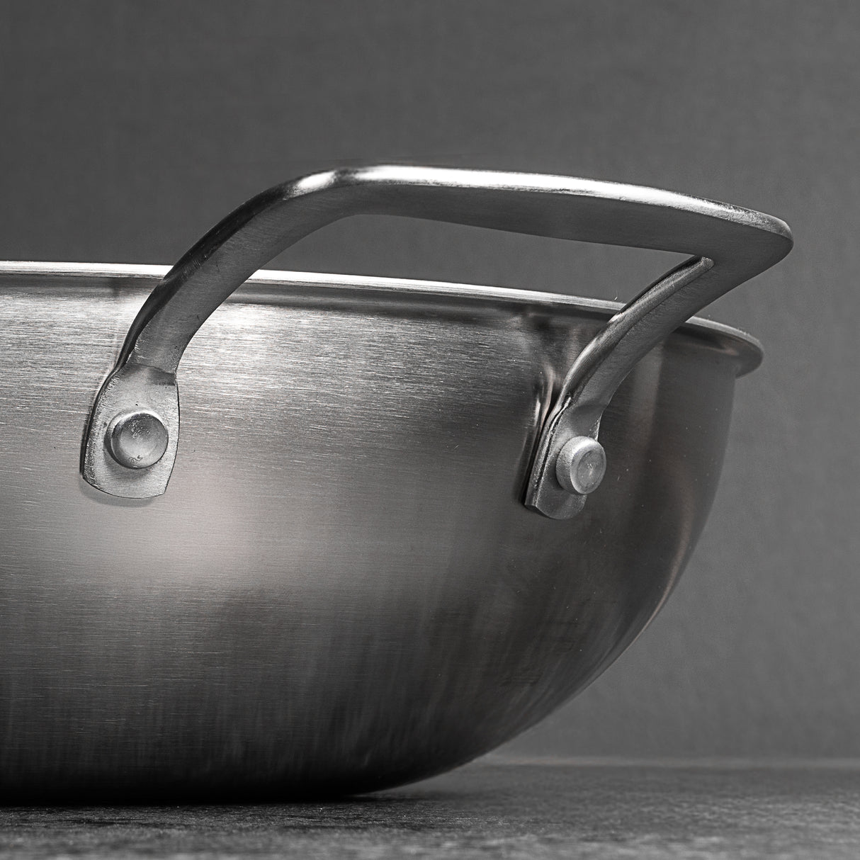 Close-up of a stainless steel wok with a handle on a grey background