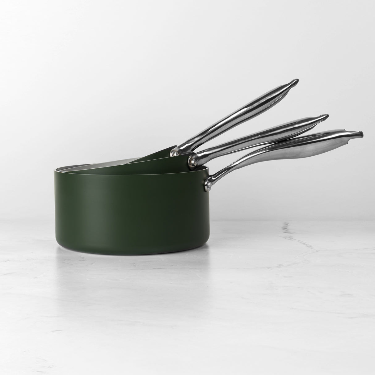 Set of three ProChef green ceramic-coated aluminium saucepans nested together, with polished stainless steel handles, displayed on a white marble surface against a plain background.