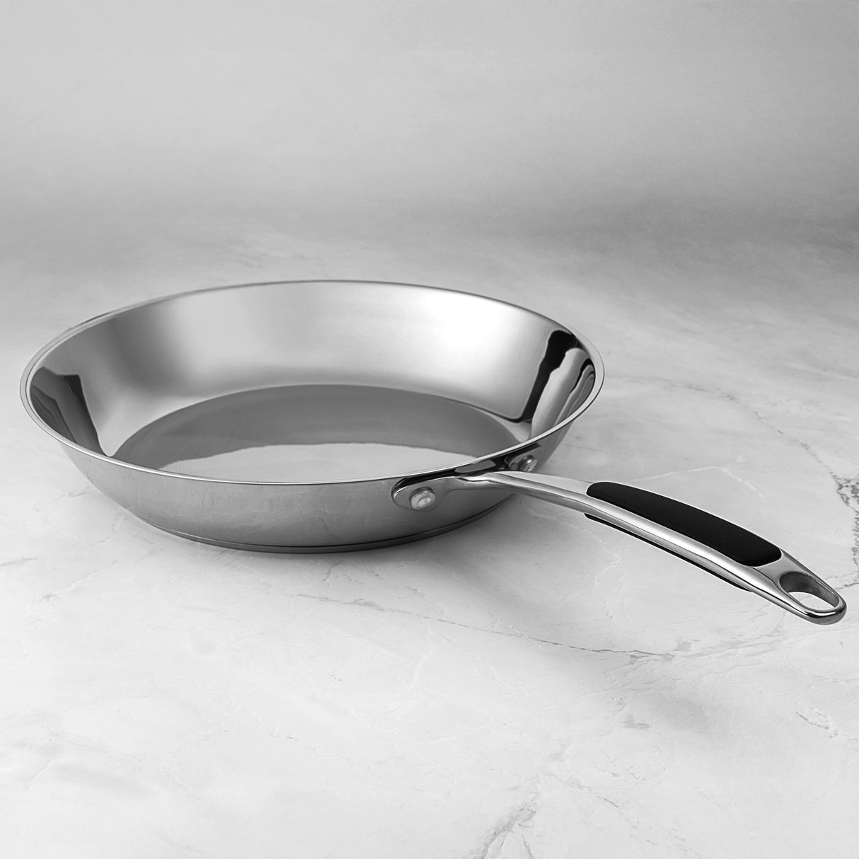 ProChef stainless steel frying pan with ergonomic handle and mirror-polished finish, displayed on a marble surface.
