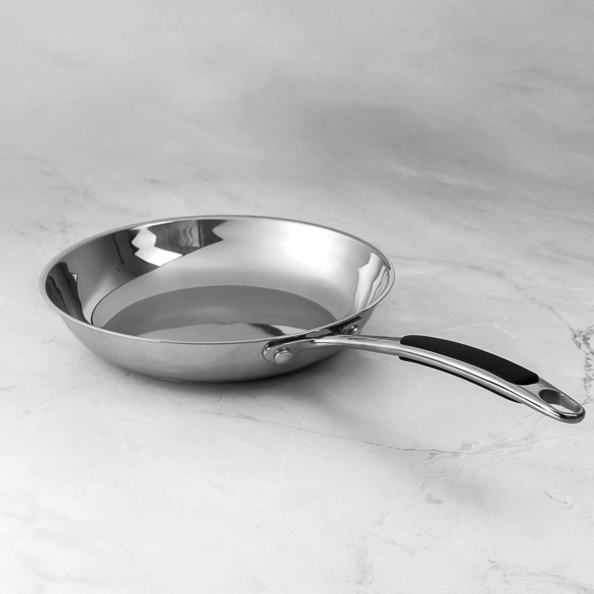ProChef stainless steel frying pan with ergonomic handle and mirror-polished finish, displayed on a marble surface.