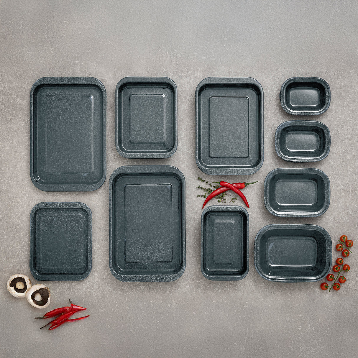 Set of grey enamel rectangular trays on a grey surface with red peppers and mushrooms.