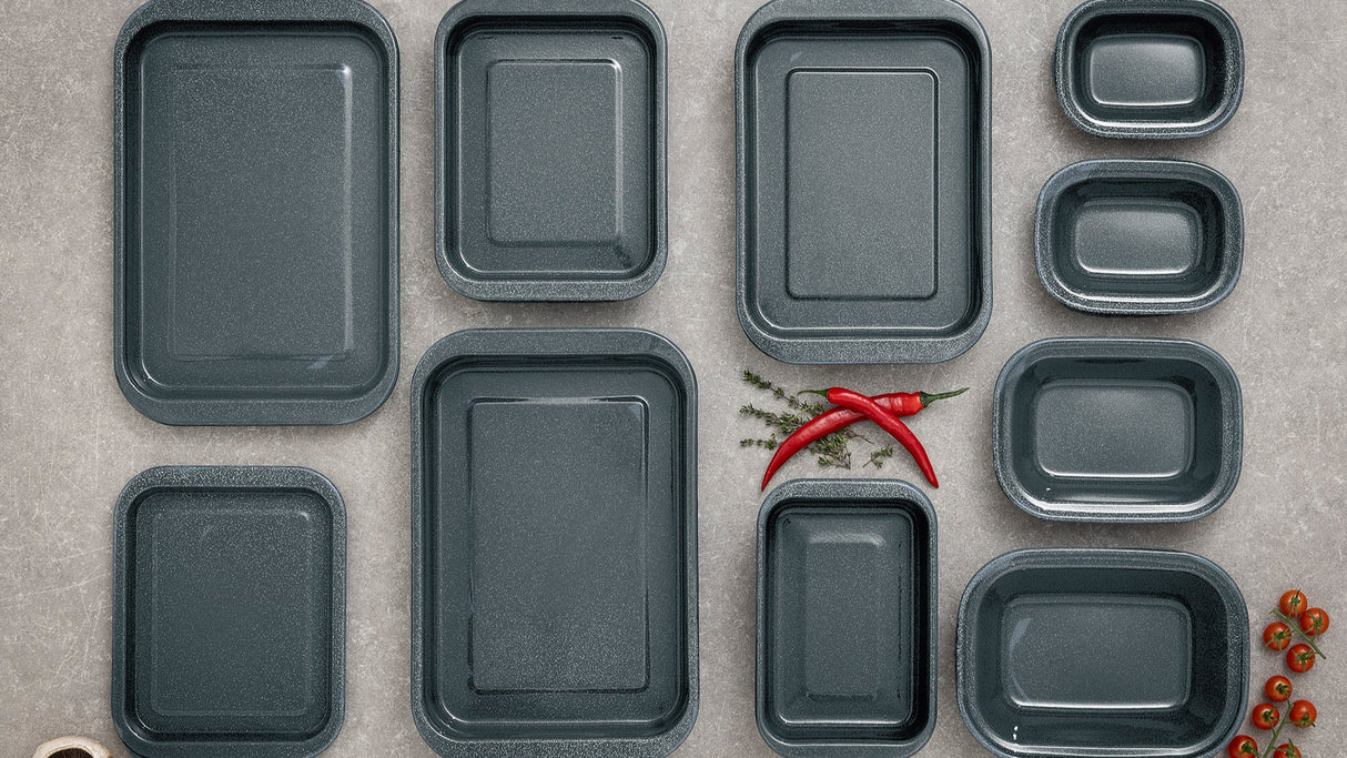 Set of grey enamel rectangular trays on a grey surface with red peppers and mushrooms.