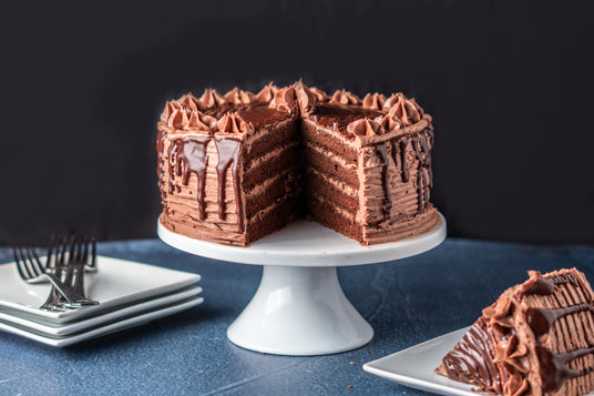 Chocolate cake on a white stand with a slice taken out, on a dark background