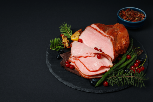 Sliced ham on a black slate plate with garnishes on a dark background