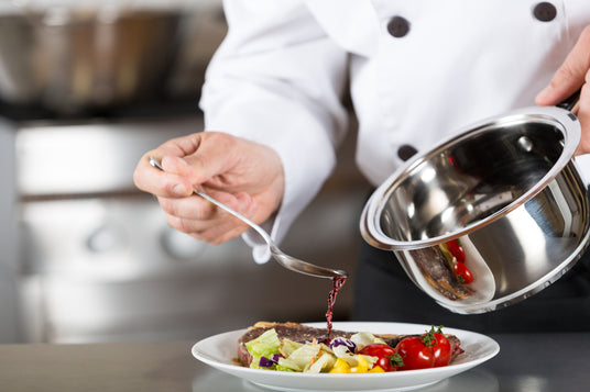 Chef garnishing a dish with a ladle in a kitchen setting