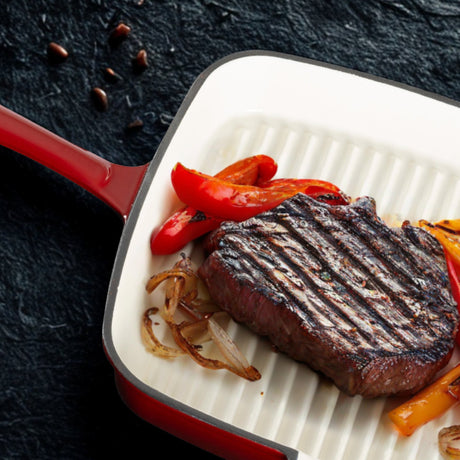 Grilled steak with peppers and onions in a red cast iron grill pan on a dark background.
