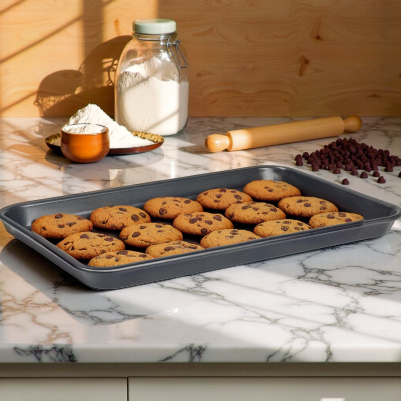 Baking tray with chocolate chip cookies on a marble countertop with baking ingredients.