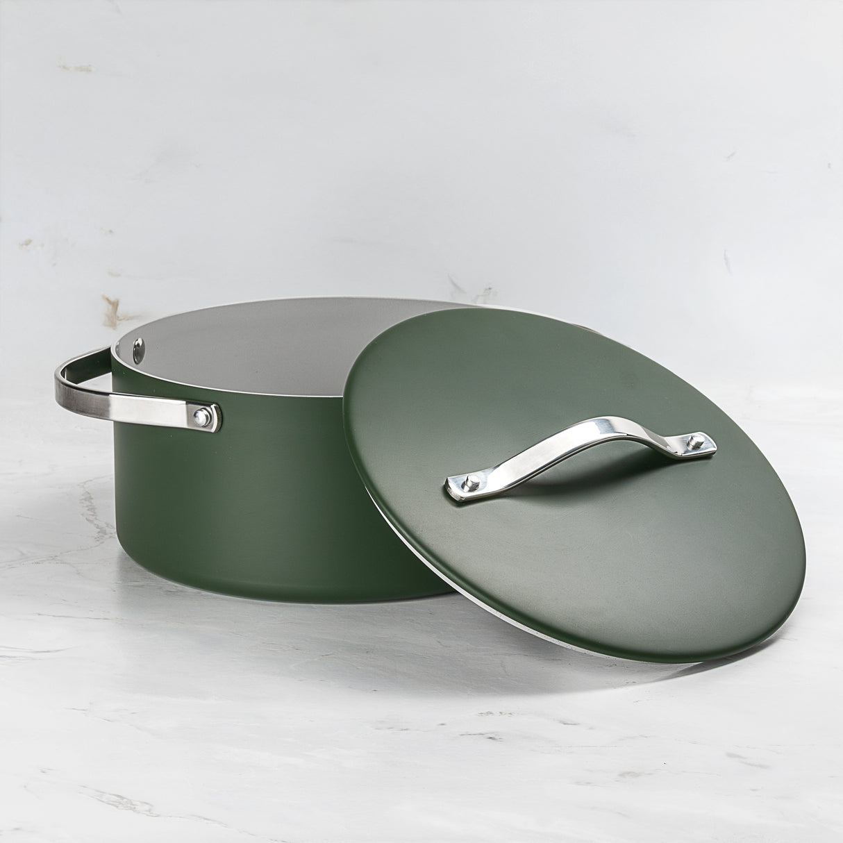 Large round green ceramic-coated aluminium casserole dish with stainless steel handles, shown with its matching lid resting slightly to the side on a marble surface.
