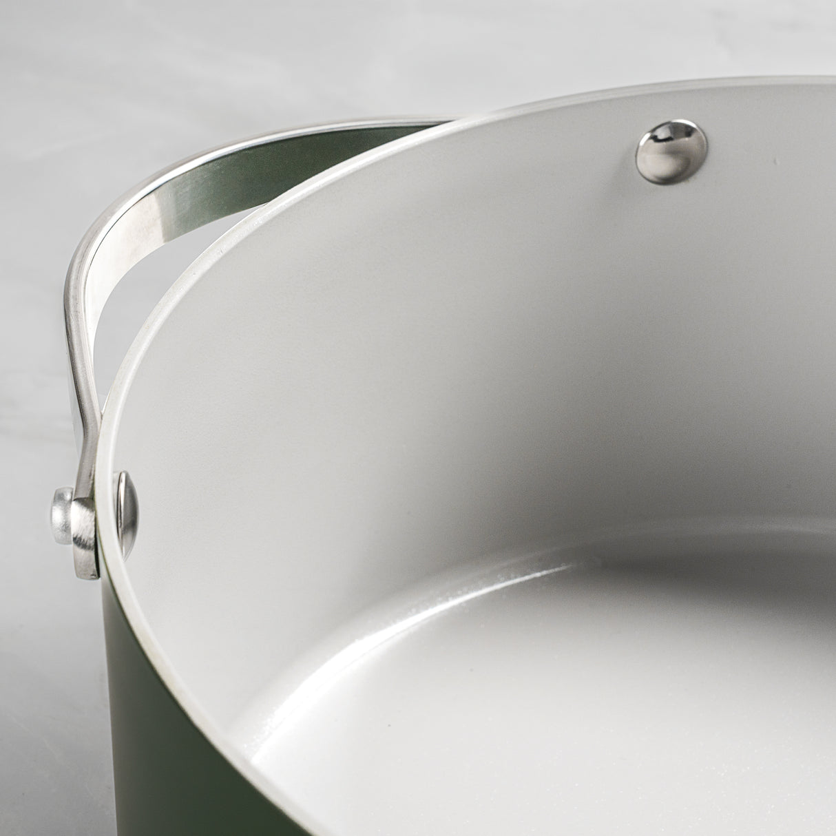 Close-up of a green pot with a silver handle on a light gray background