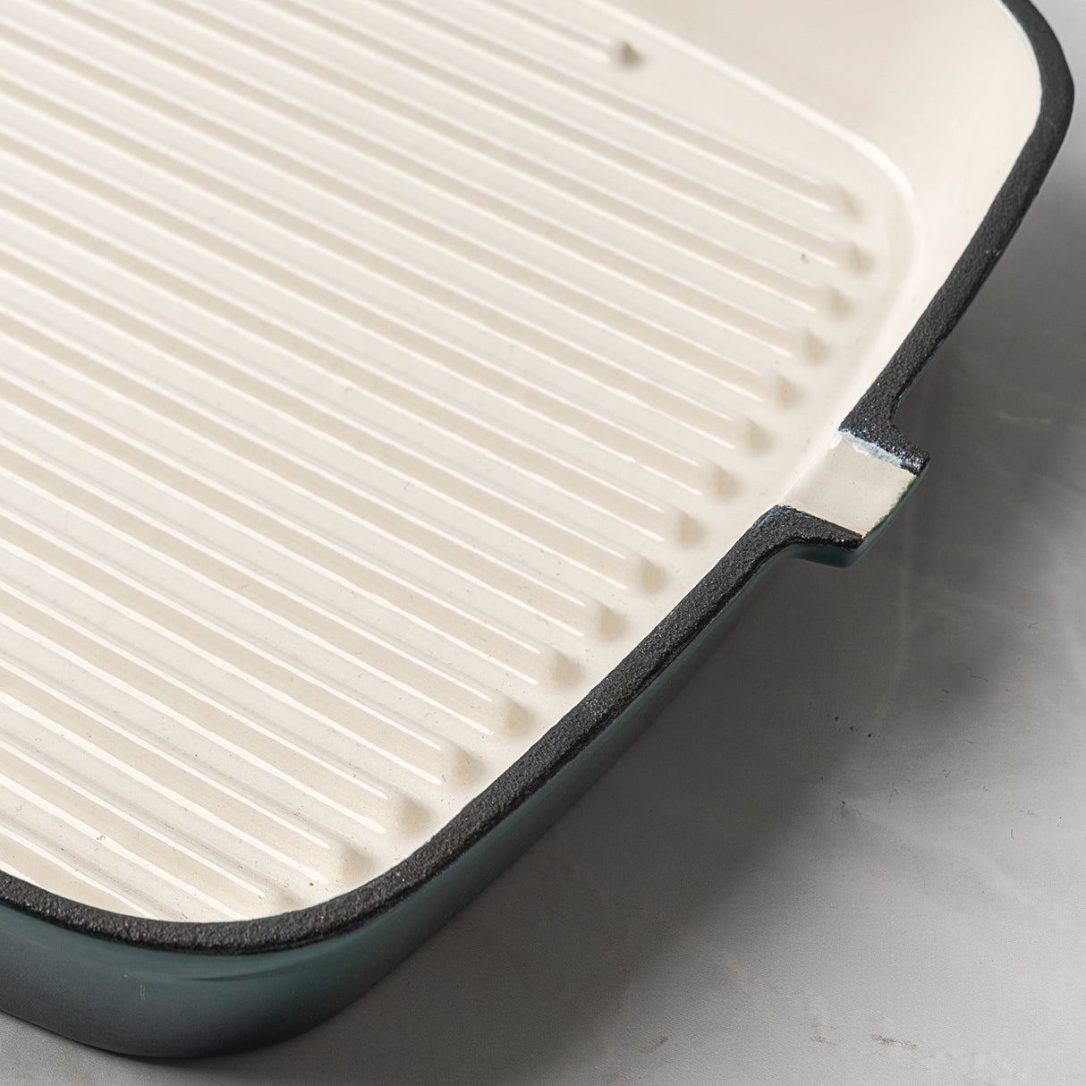 Close-up of ProChef enamelled cast iron square griddle pan in teal with cream interior and ridged base for searing.