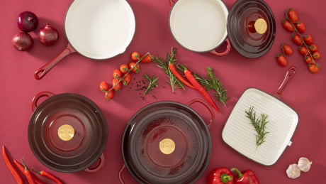 Set of deep garnet cast iron cookware on a red background with ingredients