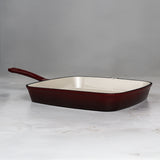 Square enameled cast iron skillet with red-brown exterior and white interior on a light gray background