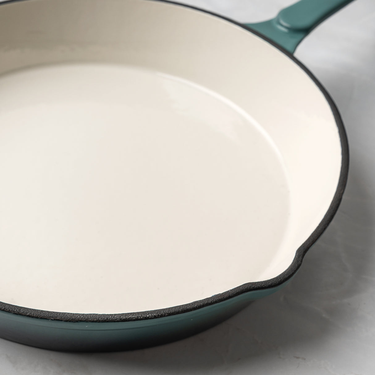 Teal enamelled cast iron skillet on a light grey background