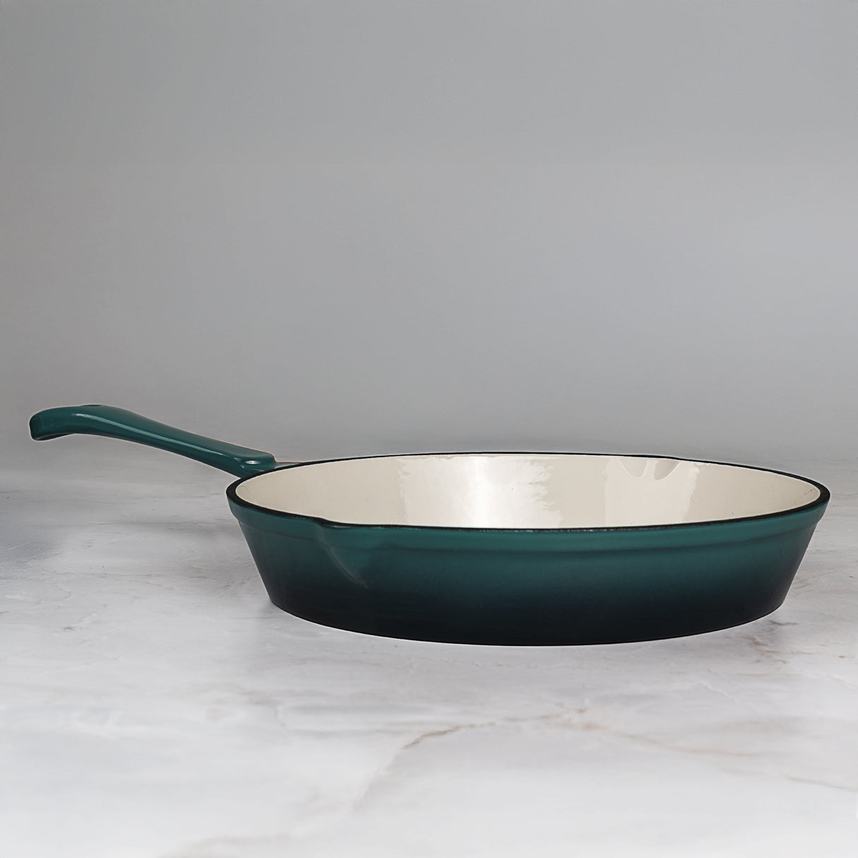 Teal cast iron frying pan on a marble surface with a grey background