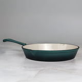Teal cast iron frying pan on a marble surface with a grey background