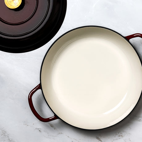 ProChef shallow cast iron casserole in deep red with white enamel interior, shown with matching lid featuring gold knob.