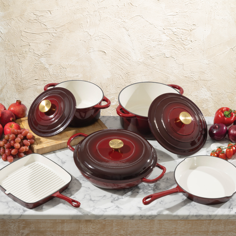 Set of ProChef red cast iron cookware with white interiors on a marble surface with fruits and vegetables.