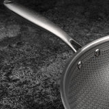 Stainless steel frying pan with geometric pattern on a dark surface