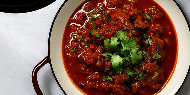 Close-up of ProChef red cast iron casserole dish filled with rich tomato stew, topped with fresh parsley.