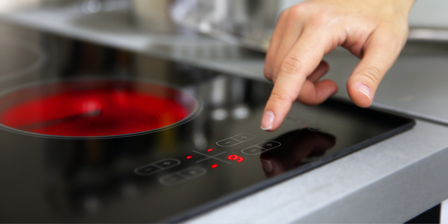 Hand pressing a button on an induction hob with a red indicator light.