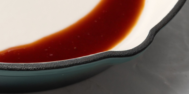 Close-up of ProChef cast iron pan with cream enamel interior showing red sauce against dark teal exterior.